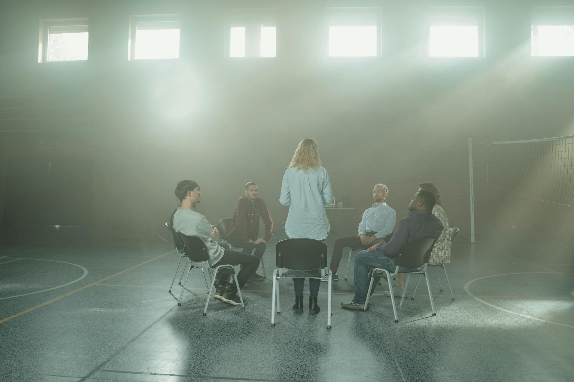 A diverse group of adults in a supportive group session, seated in a circle in a warm, sunlit room